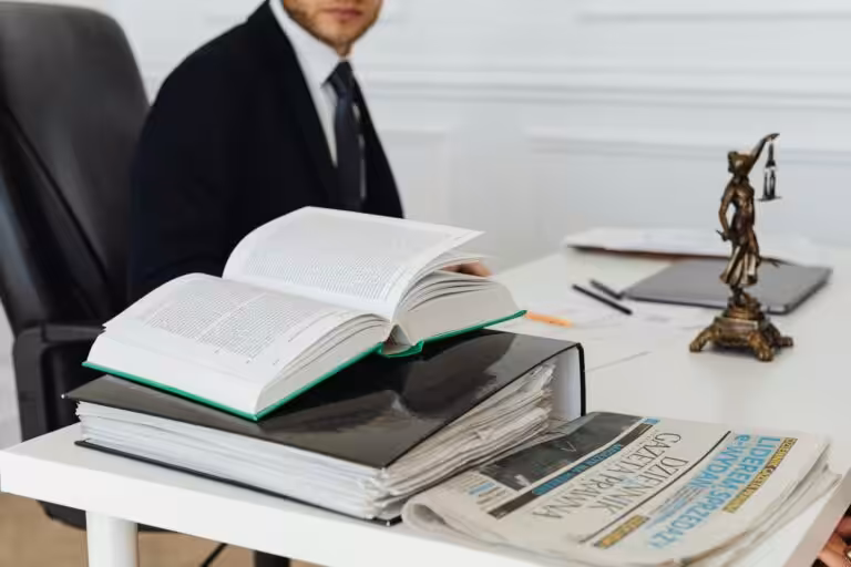 Person seated with several books, a pen, a newspaper, and a justice statue