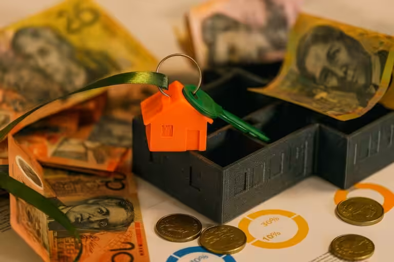 Paper bills and coins on a table beside a miniature house and key symbolising upfront fees