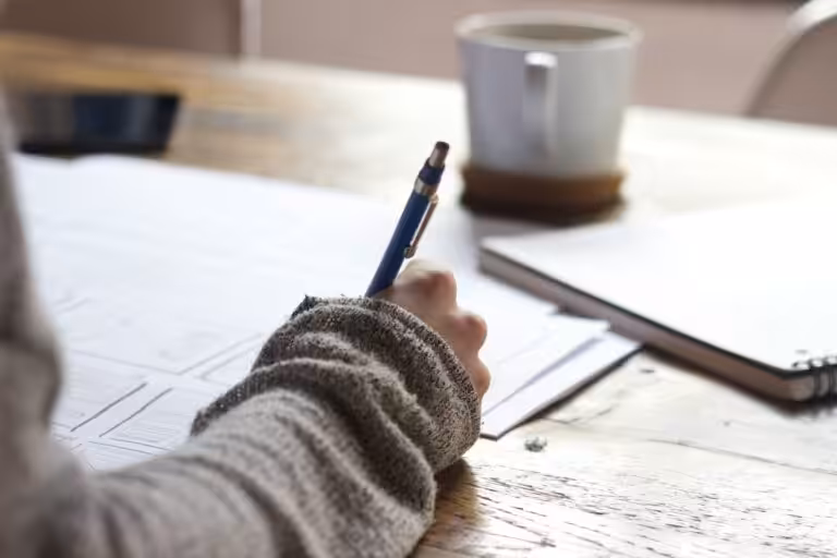 Person holding a pen and writing on legal documents with a cup in front